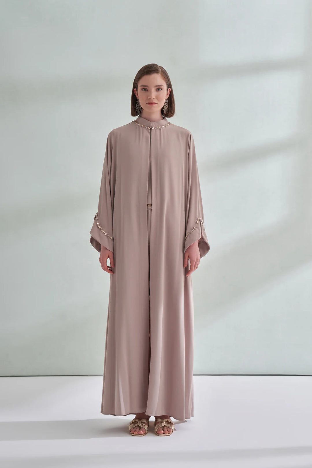 Woman wearing a long, light brown dress against a plain background