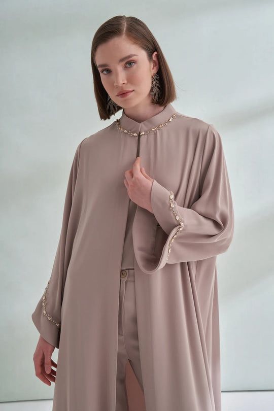 Woman wearing a long beige dress with intricate detailing on a plain background