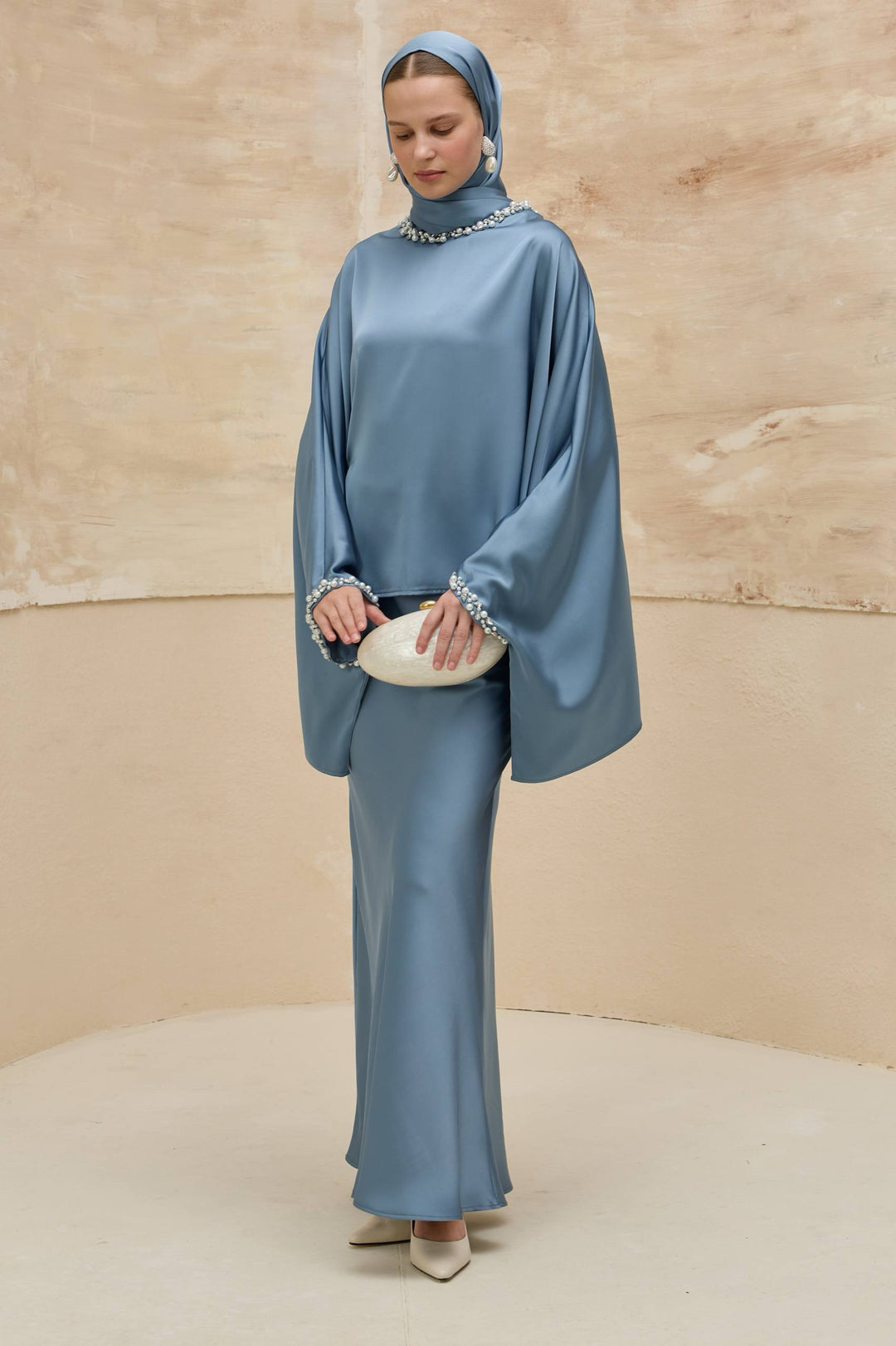 Woman wearing a blue outfit with a headscarf against a beige background