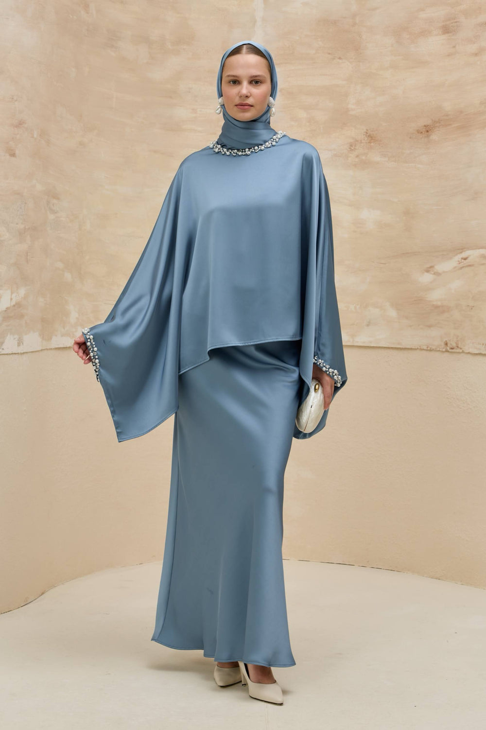 Woman wearing a blue outfit with a matching headscarf against a beige background