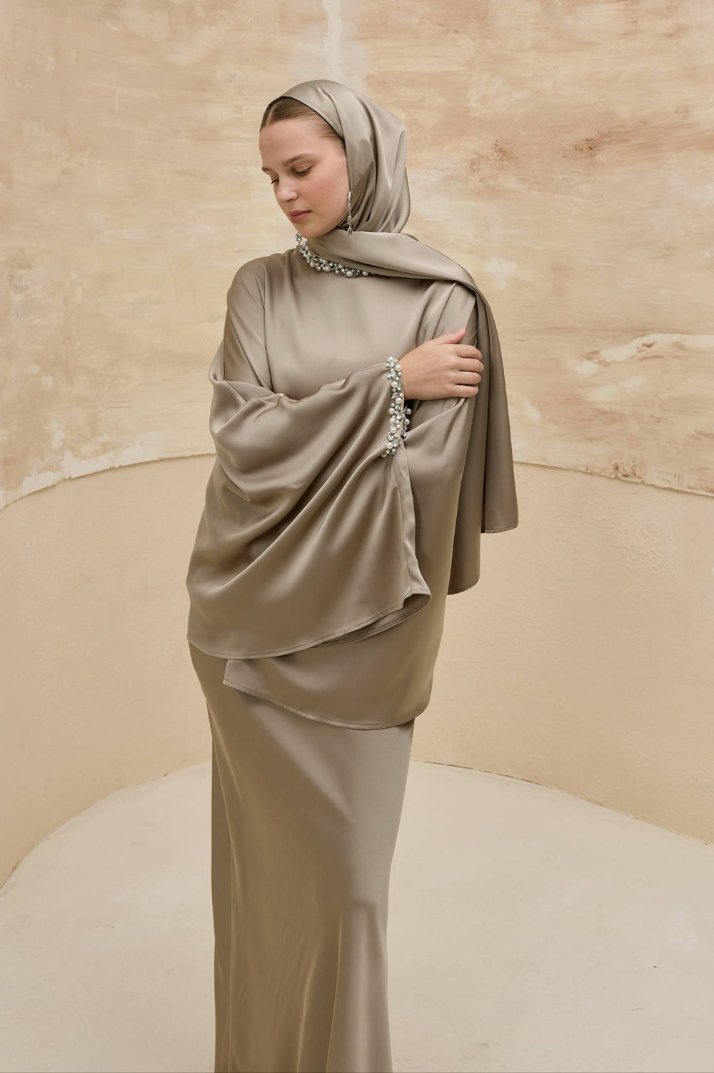 Woman wearing a beige hijab and dress against a beige background