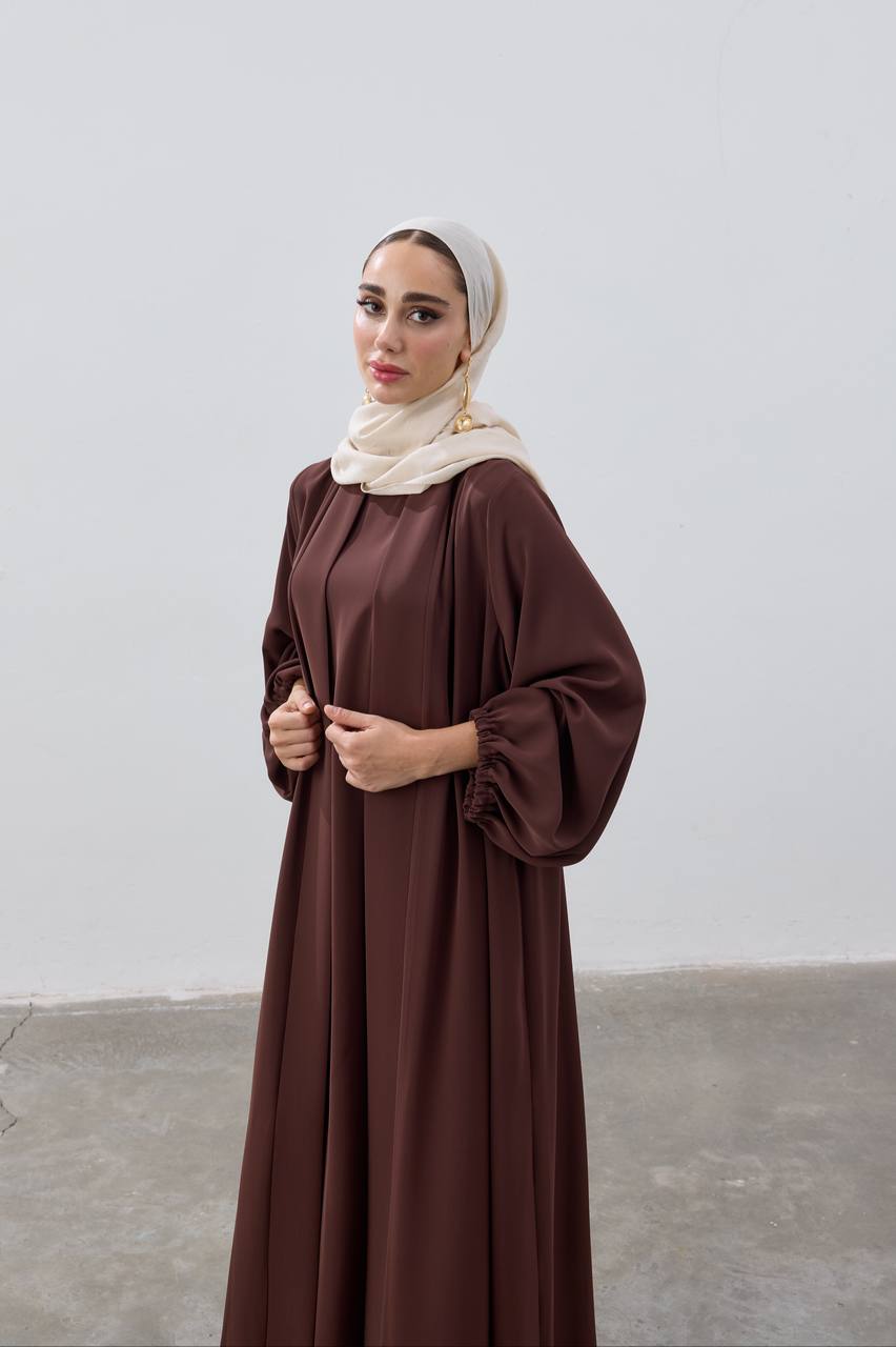 Woman wearing a brown dress and beige hijab against a plain background
