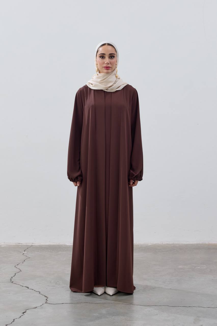 Woman wearing a long brown dress and beige hijab on a white background