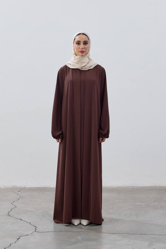Woman wearing a long brown dress and beige hijab on a white background