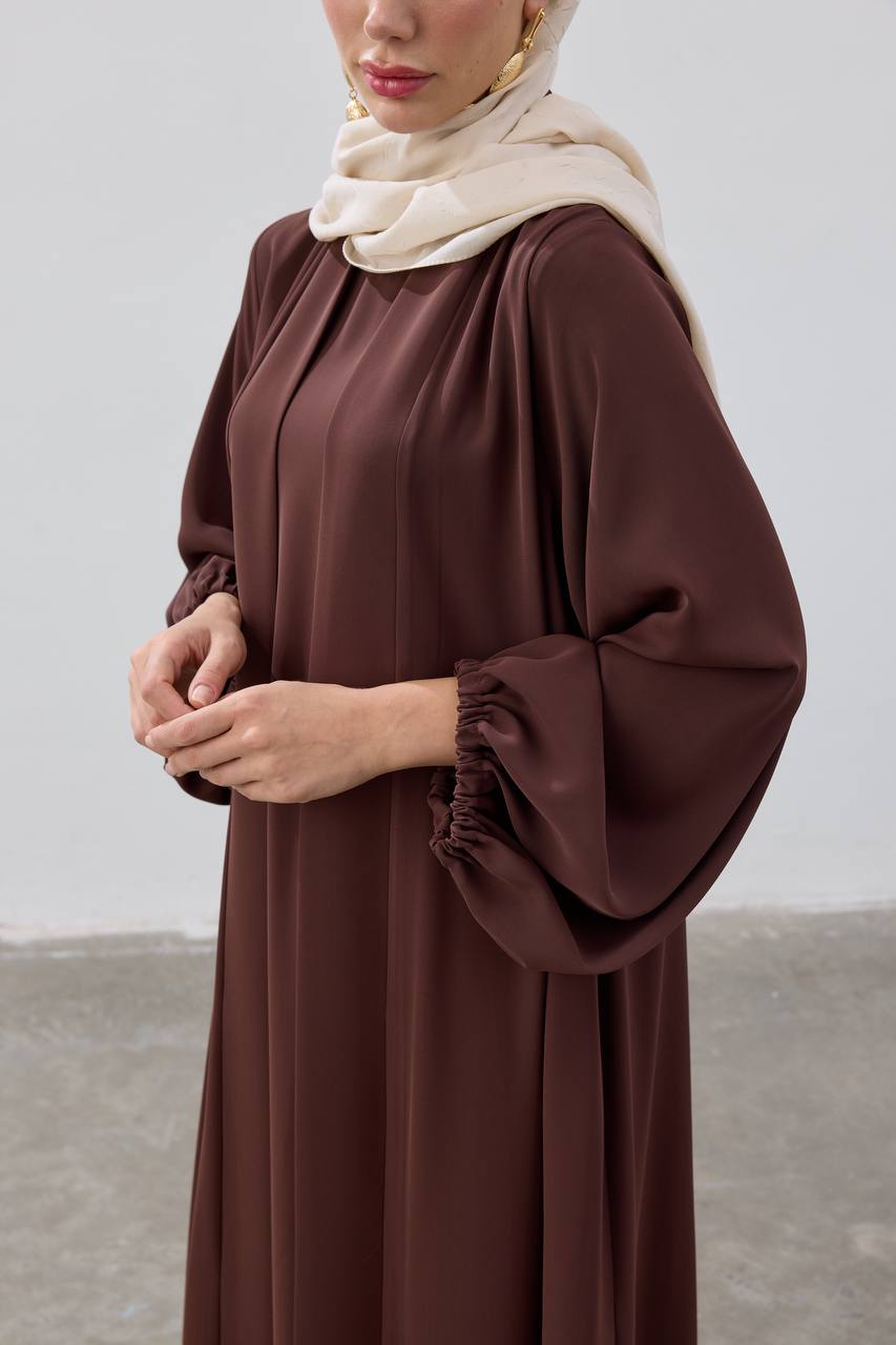 Woman wearing a brown dress with a beige hijab against a plain background