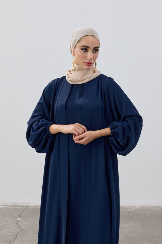 Woman wearing a navy blue abaya with a beige hijab against a white background
