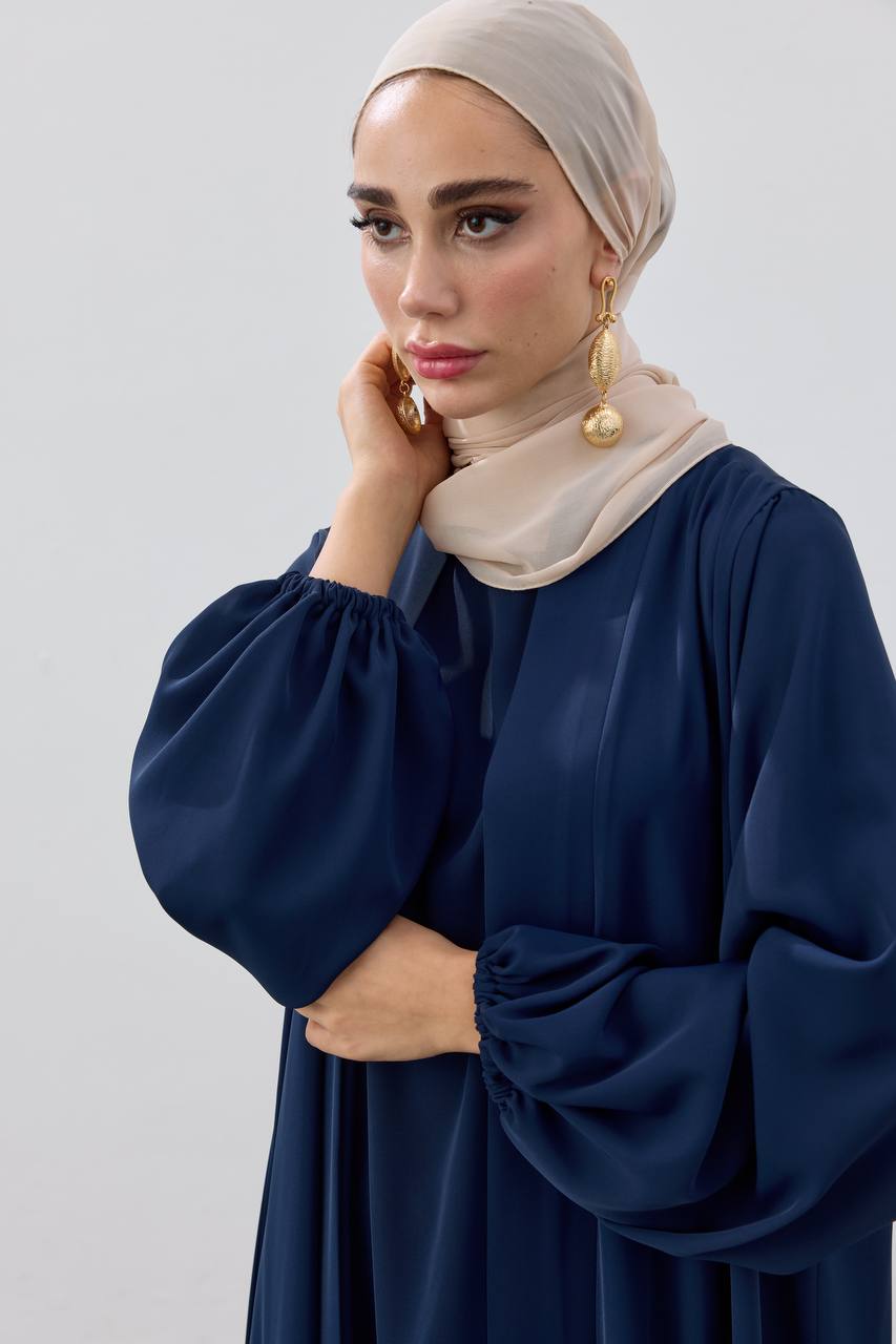 Woman wearing a navy blue dress with beige hijab against a light gray background