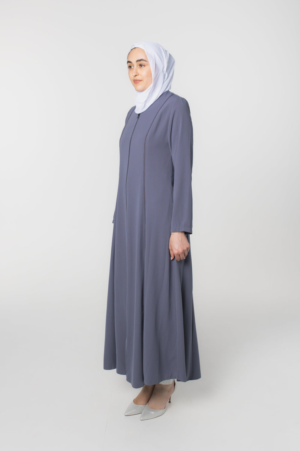 Woman wearing a long gray dress and white hijab on a white background