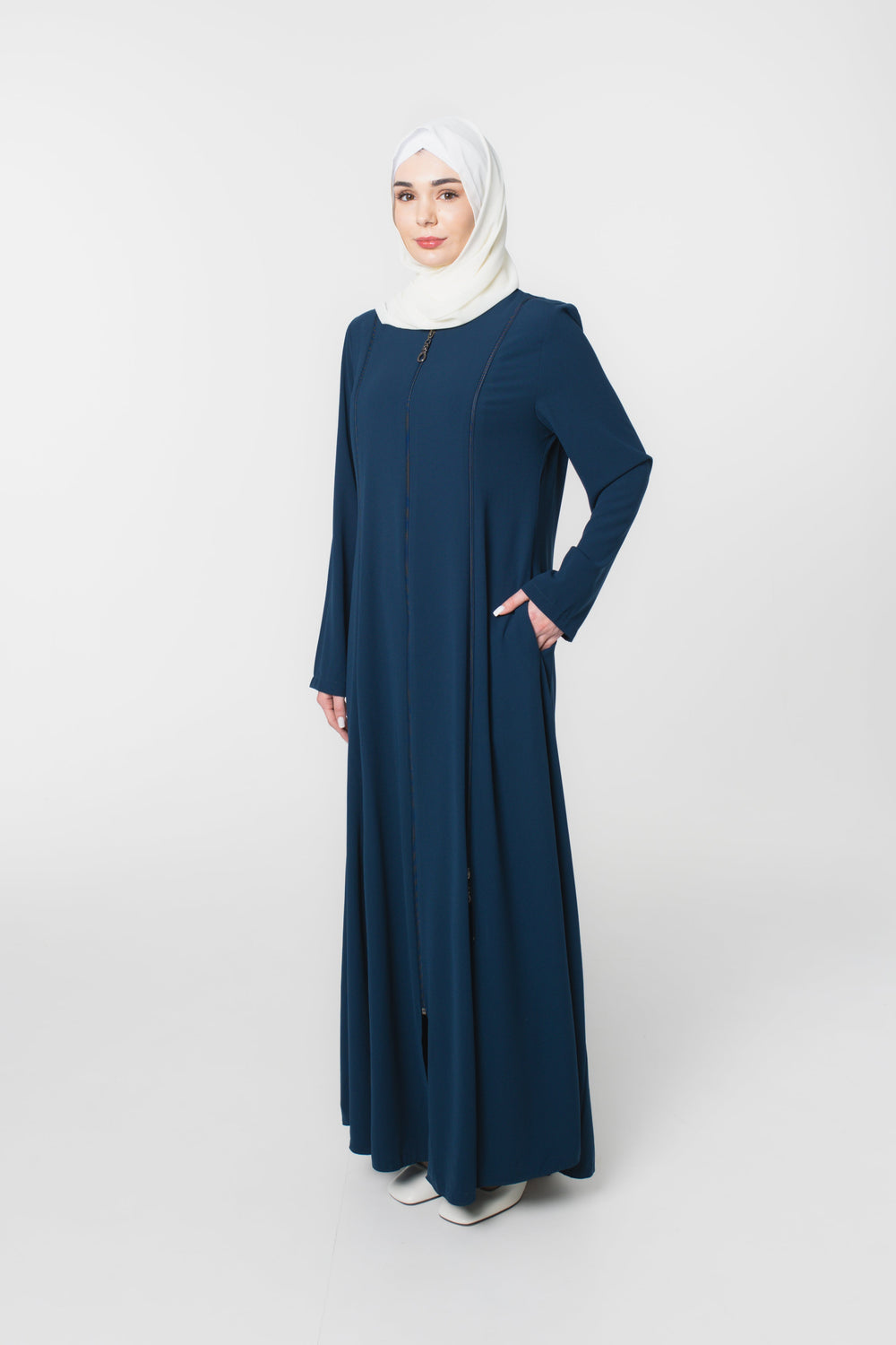 Woman wearing a long navy blue dress with a white hijab on a white background