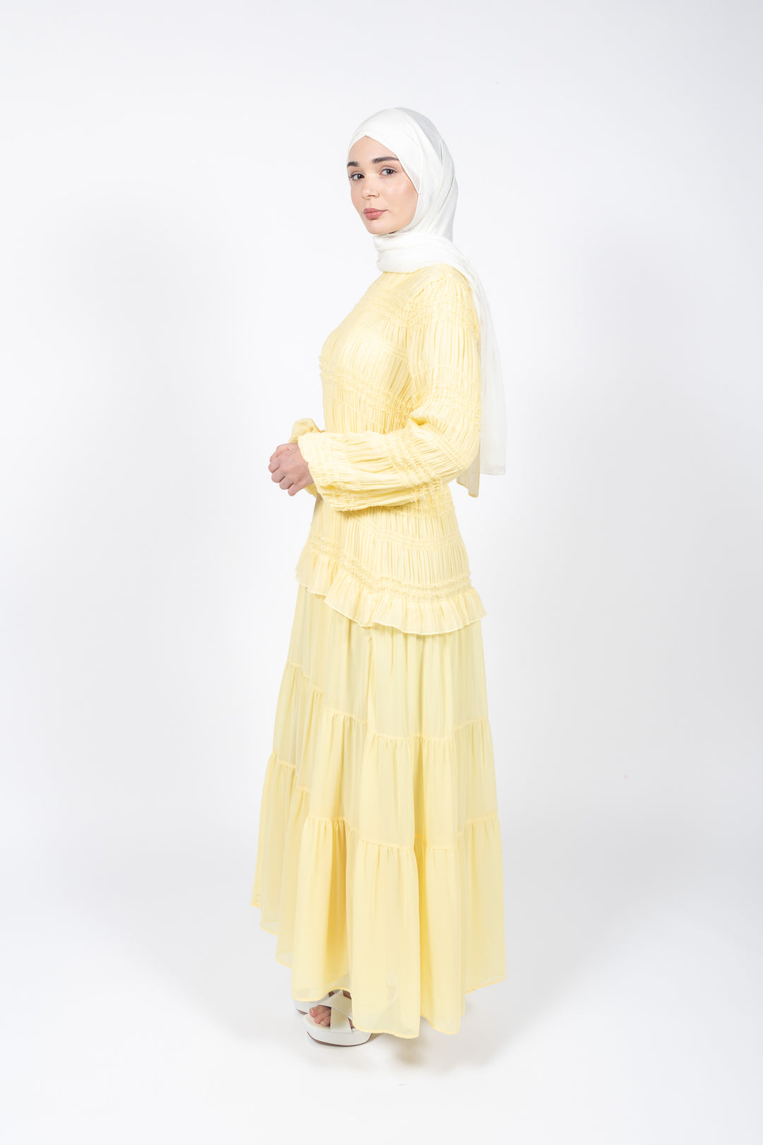 Woman wearing a yellow dress and white hijab on a white background