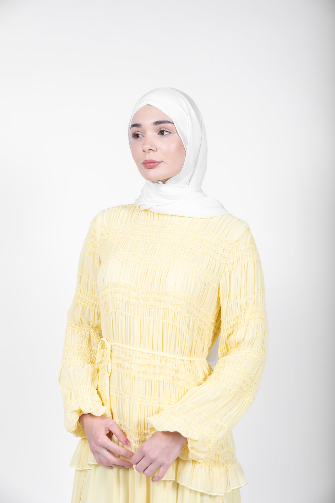 Woman wearing a yellow dress with a white hijab on a white background