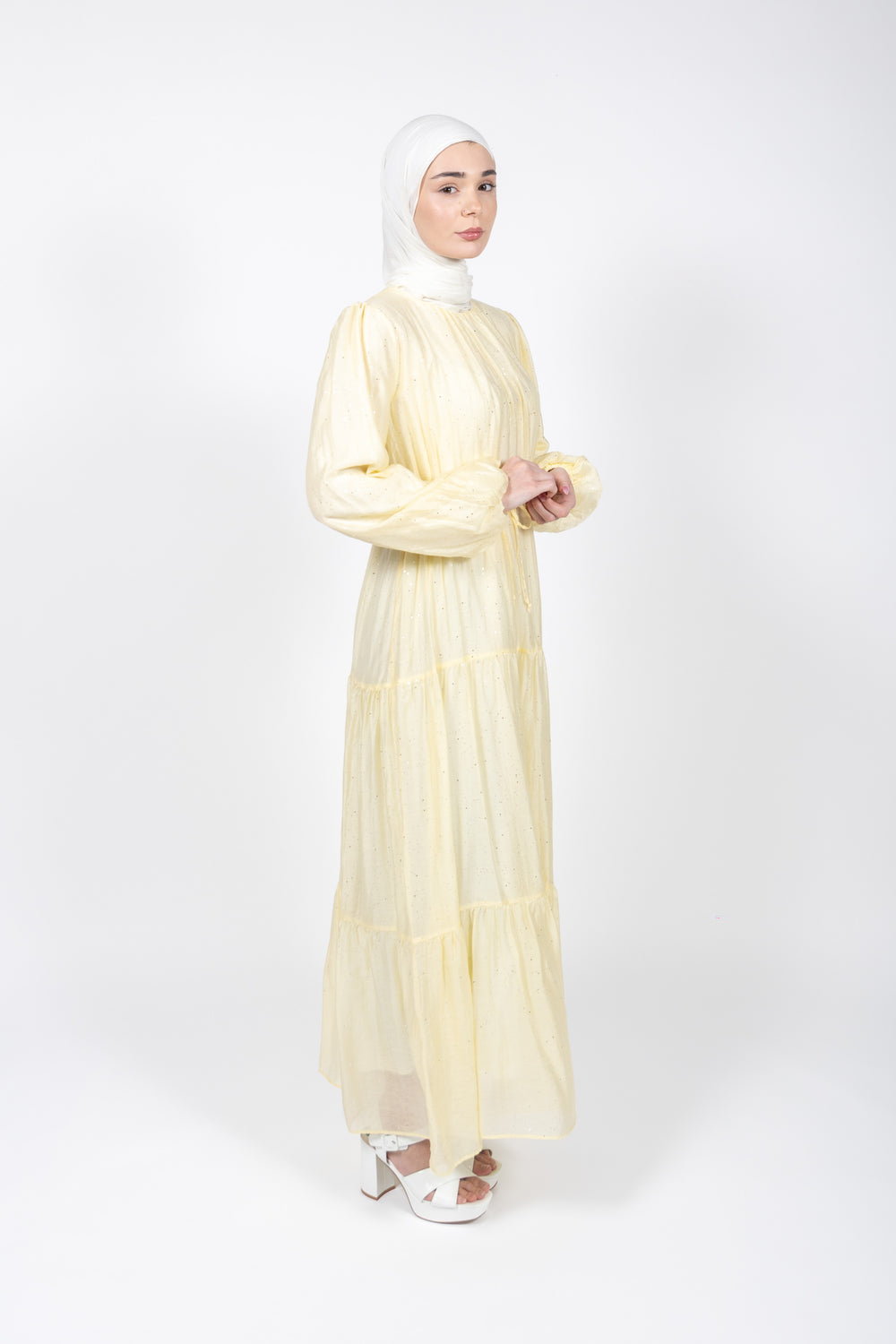Woman wearing a light yellow dress and hijab on a white background