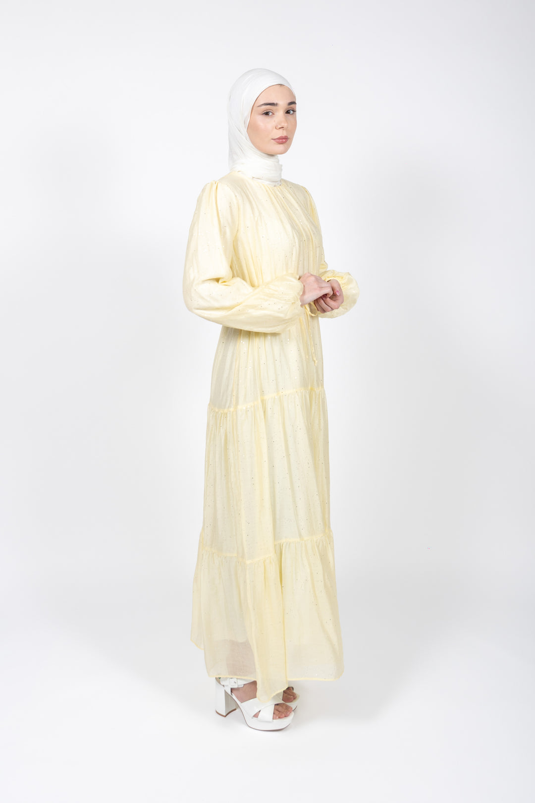 Woman wearing a light yellow dress and hijab on a white background