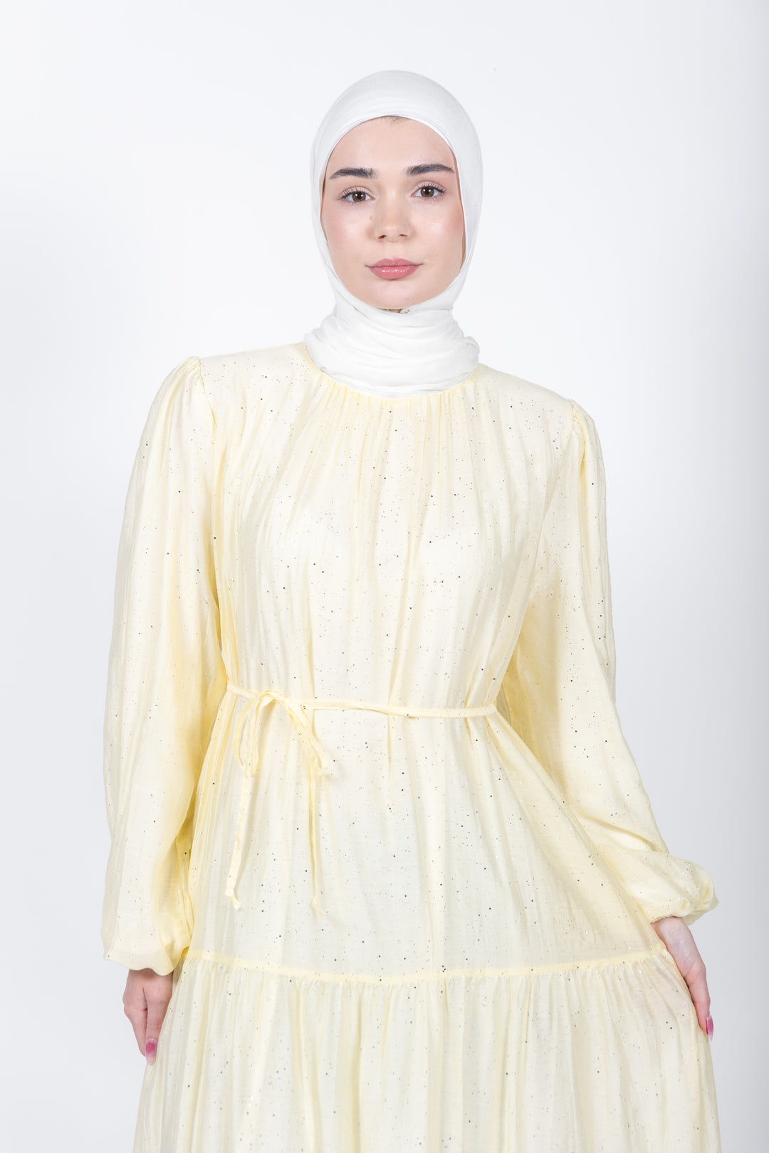 Woman wearing a light yellow dress with long sleeves and a white hijab on a white background