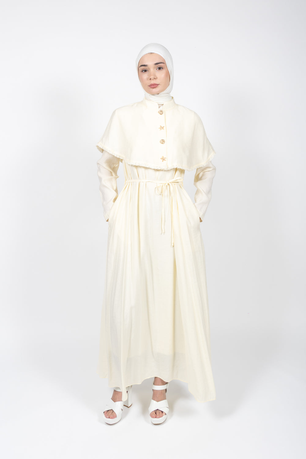 Woman wearing a long, light-colored dress with a matching hijab on a white background