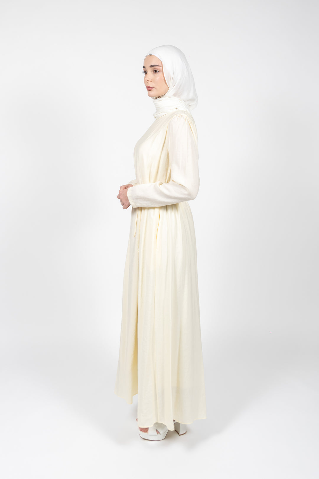 Woman wearing a long, light-colored dress with a hijab on a white background