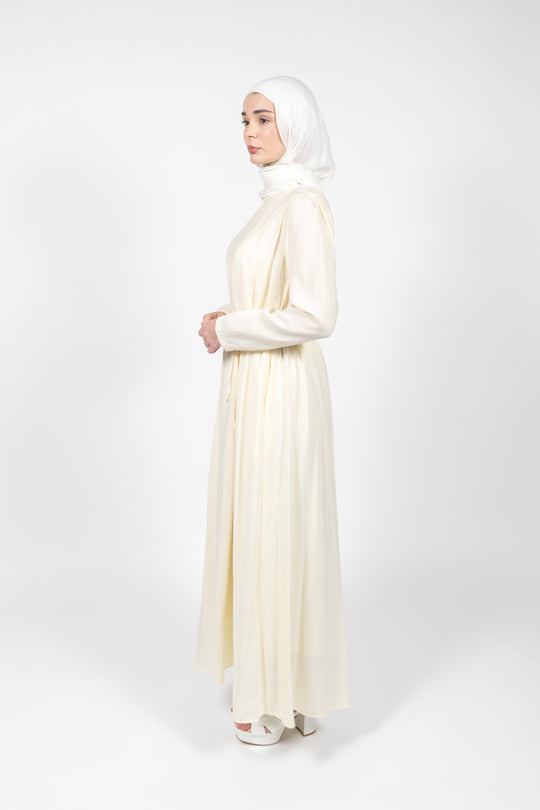 Woman wearing a long, light-colored dress with a hijab on a white background