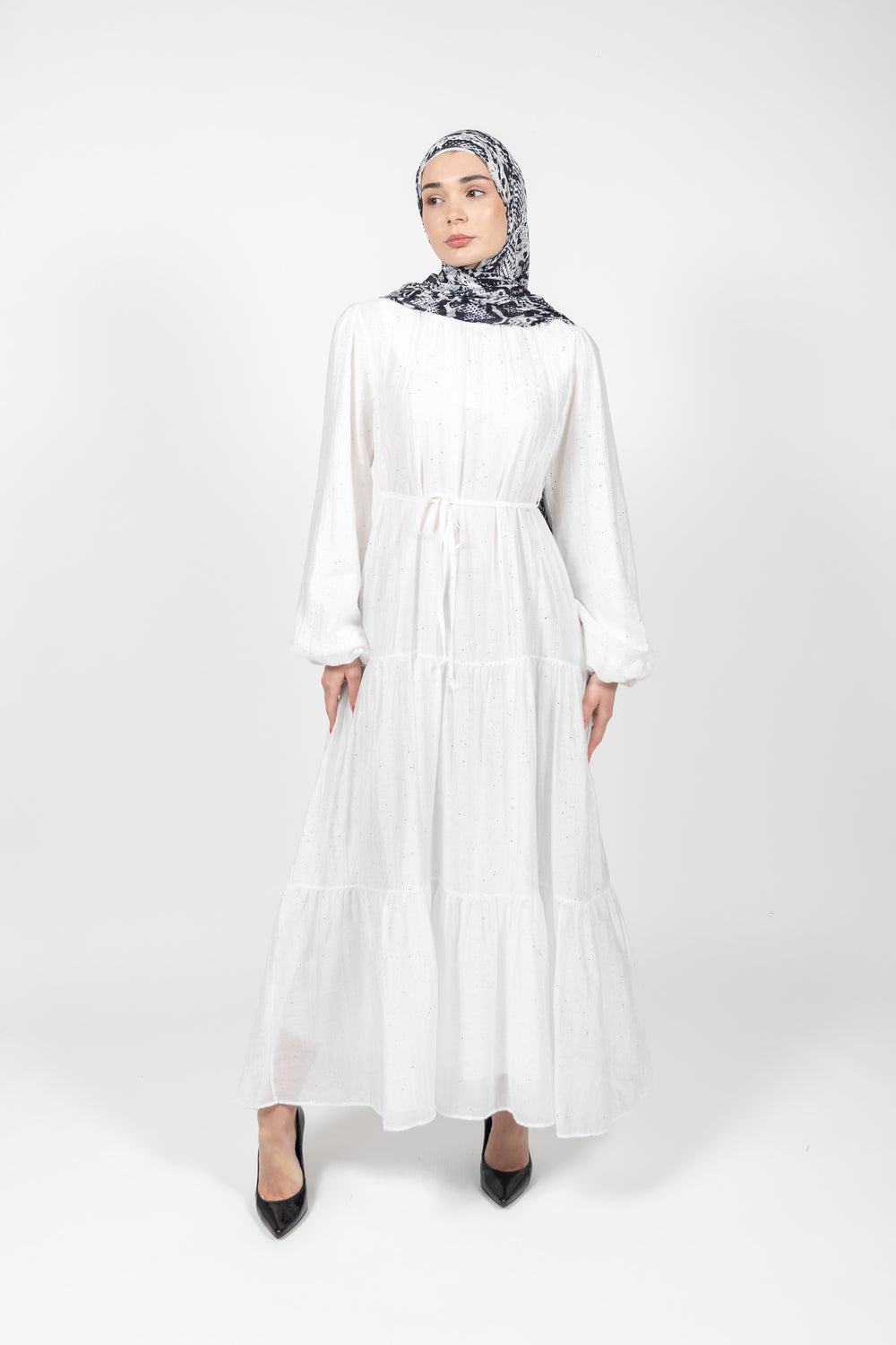 Woman wearing a white dress and patterned hijab on a white background