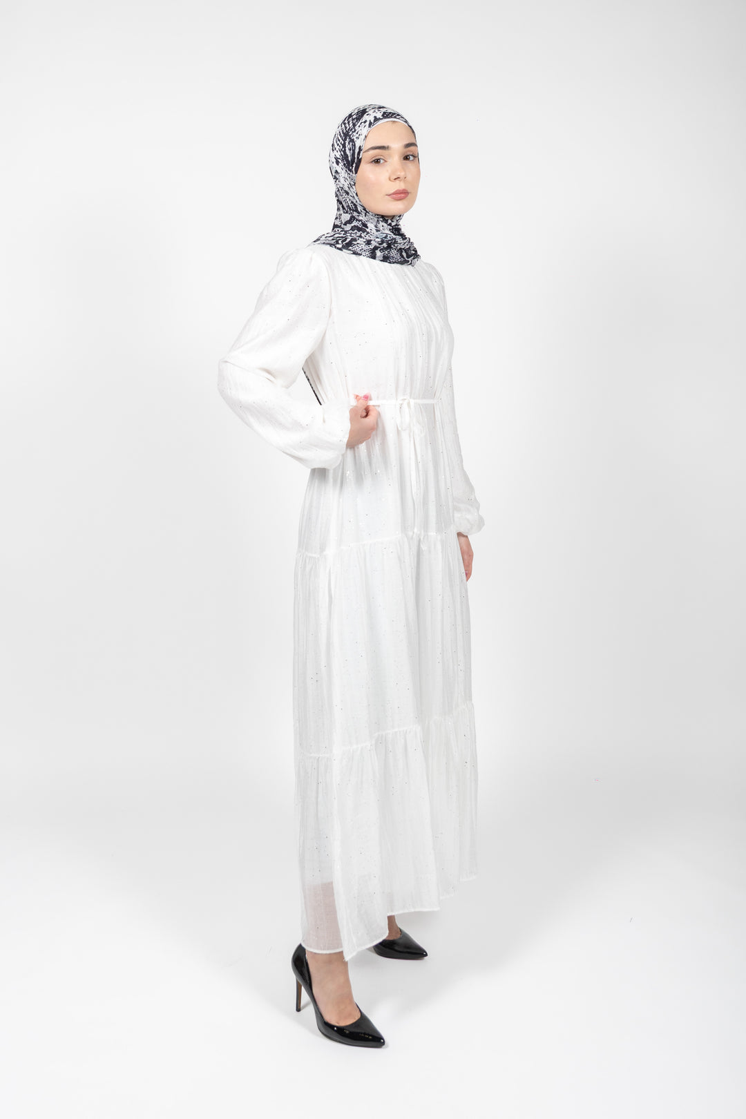 Woman wearing a white dress and patterned hijab on a white background