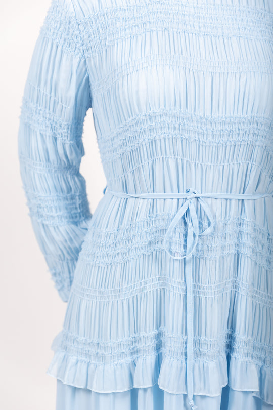 Light blue dress with smocked bodice and ruffled layers on a white background
