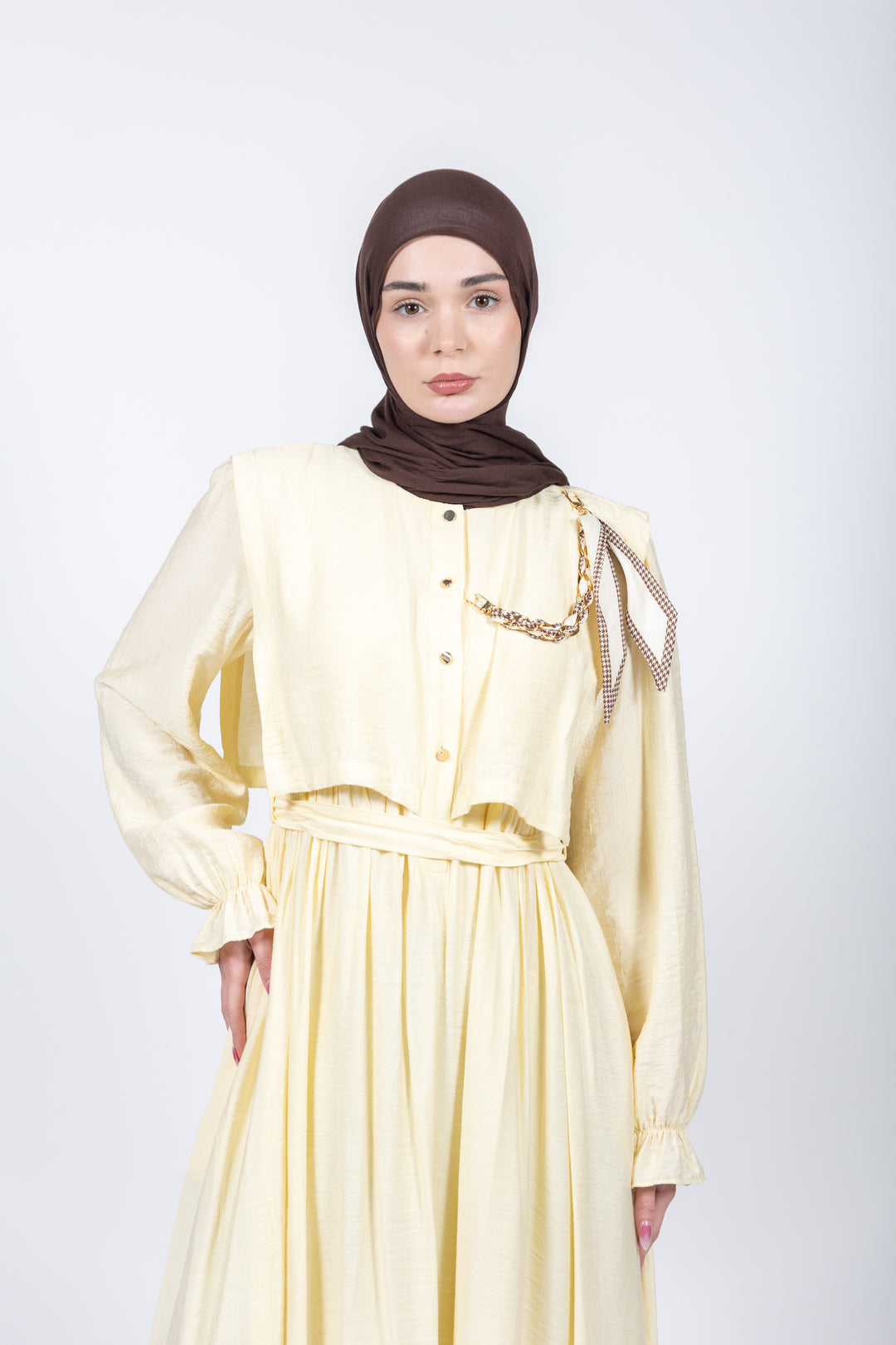 Woman wearing a light yellow dress with a brown hijab on a white background