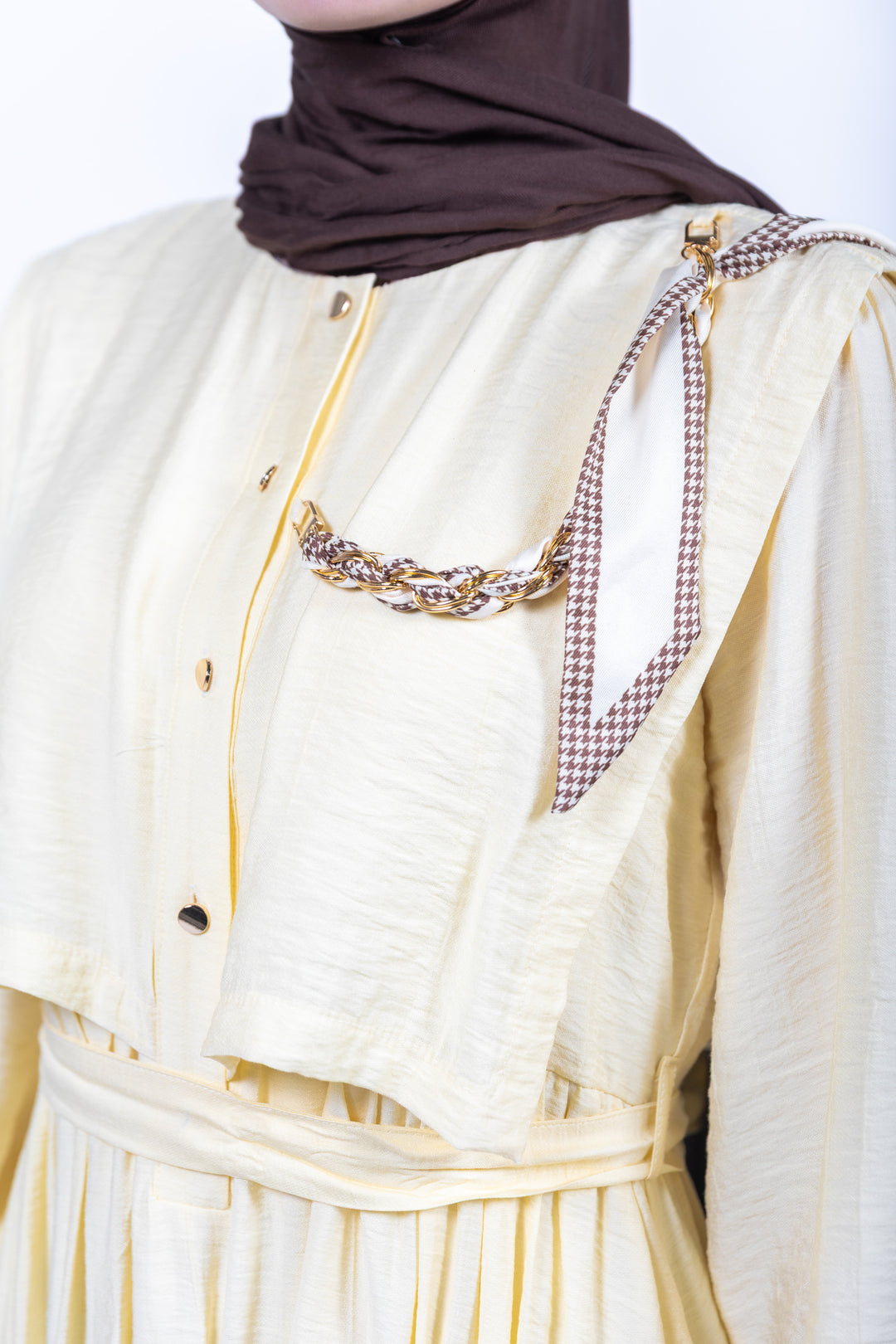 Person wearing a white outfit with a brown hijab and a gold necklace.