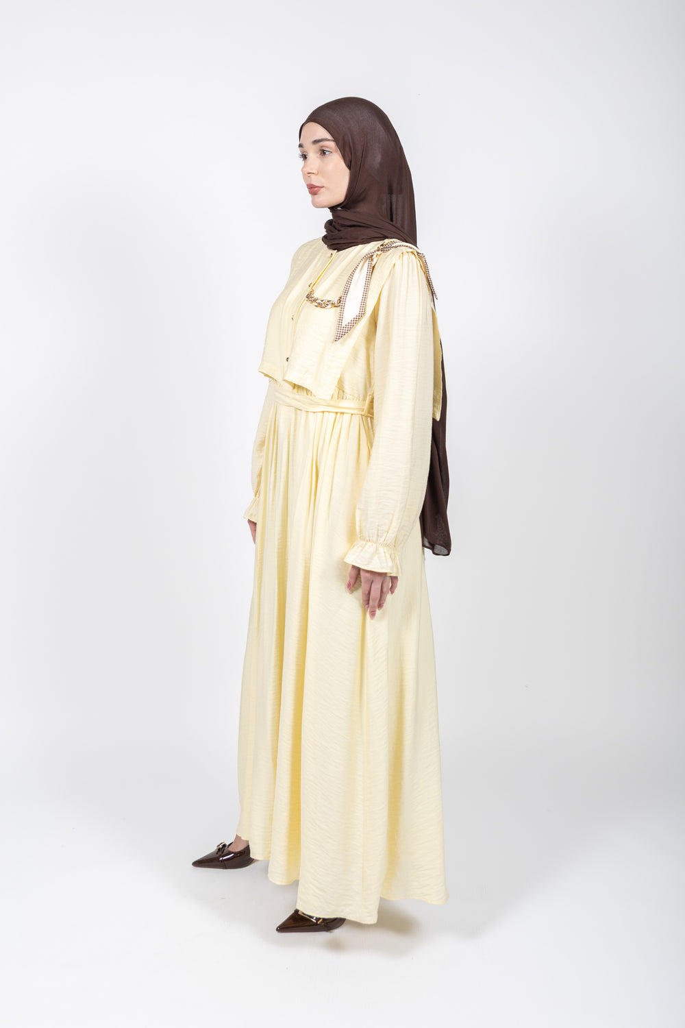 Woman wearing a long yellow dress with a brown hijab on a white background