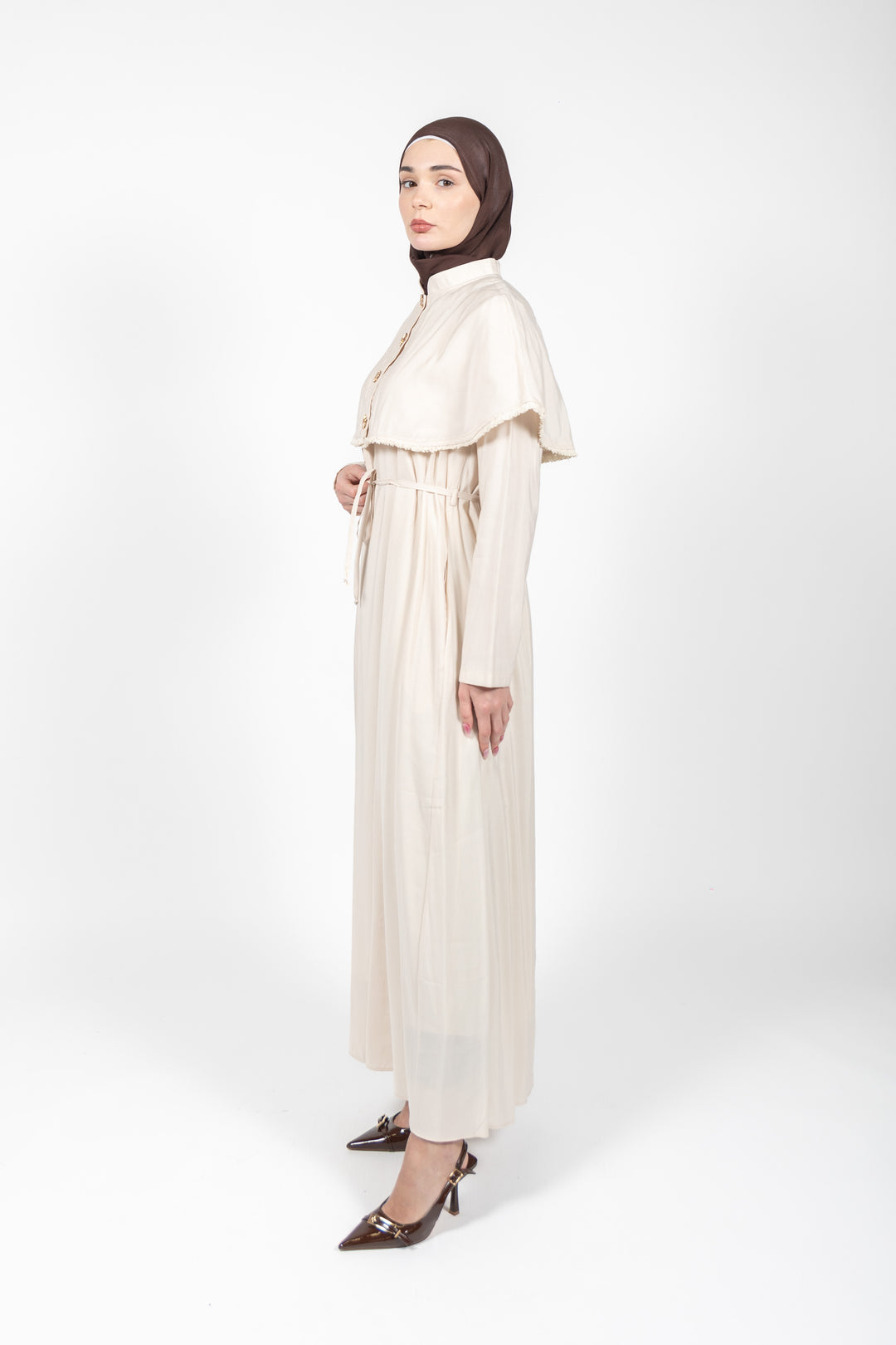 Woman wearing a long beige dress with a high collar on a white background