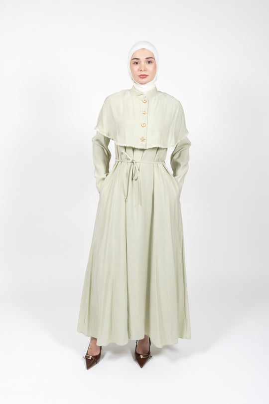 Woman wearing a light green dress with a matching hijab on a white background