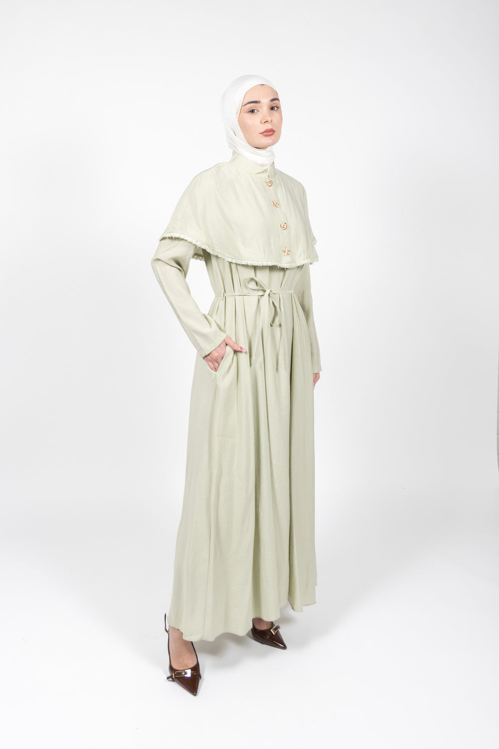 Woman wearing a light green dress with a matching hijab on a white background