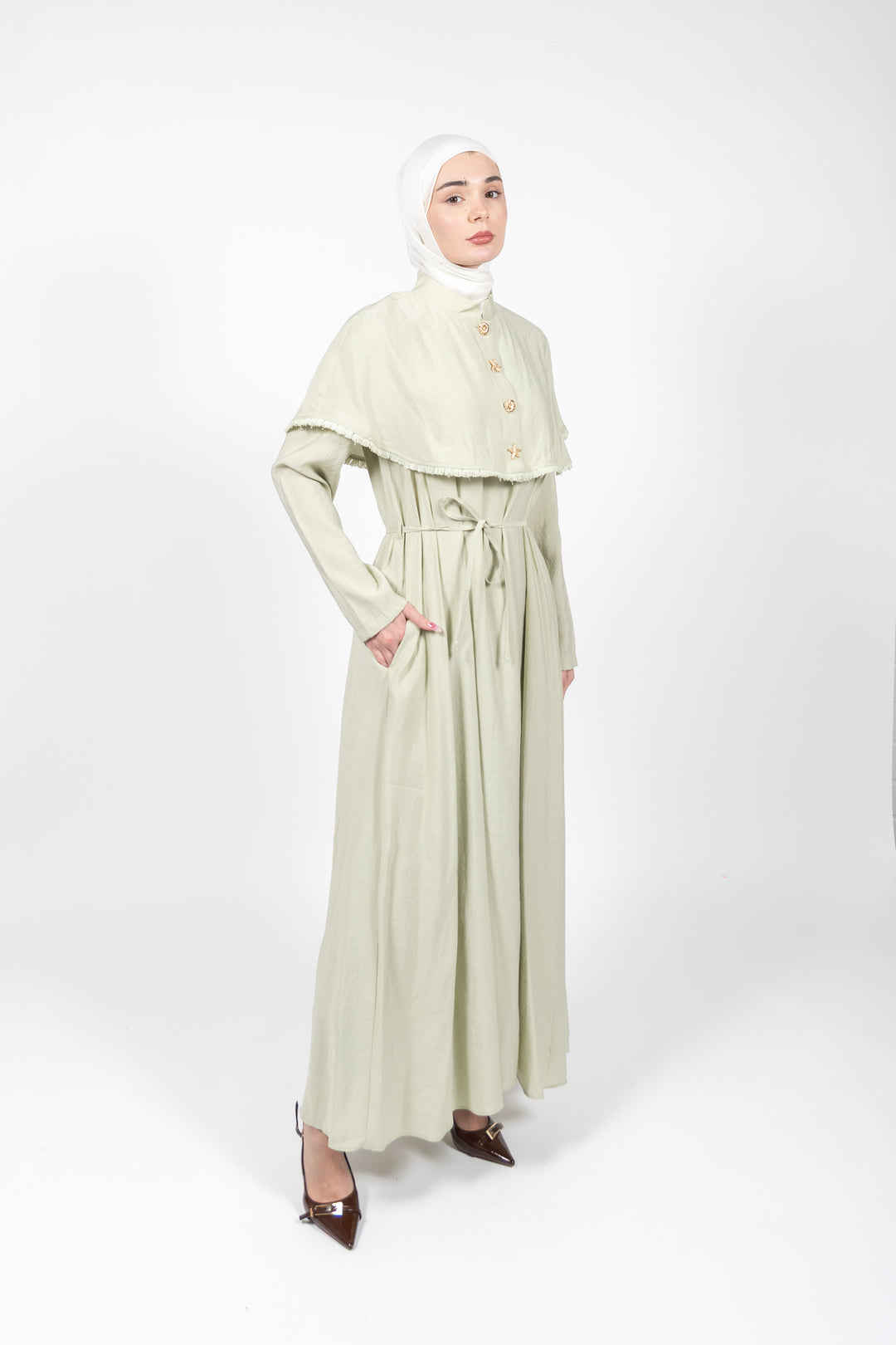 Woman wearing a light green dress with a matching hijab on a white background