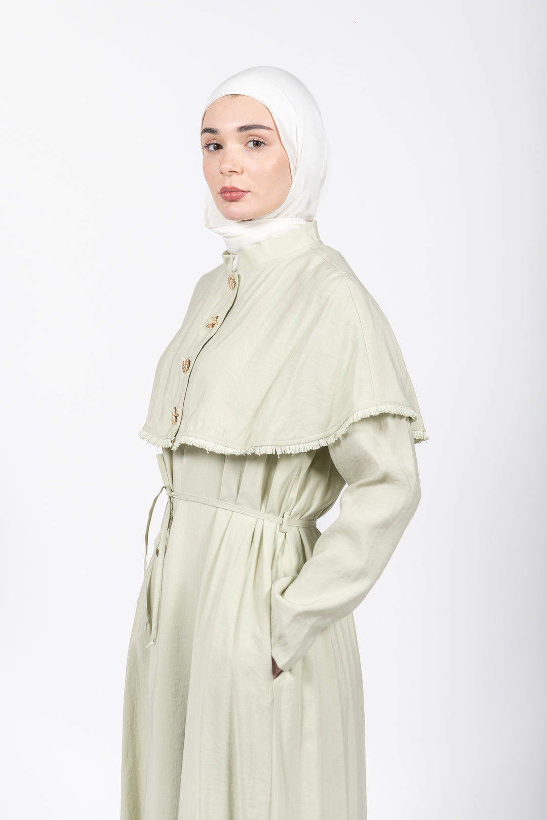 Woman wearing a light green dress with a matching headscarf on a white background