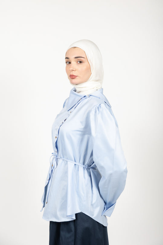 Woman wearing a light blue shirt and hijab on a white background