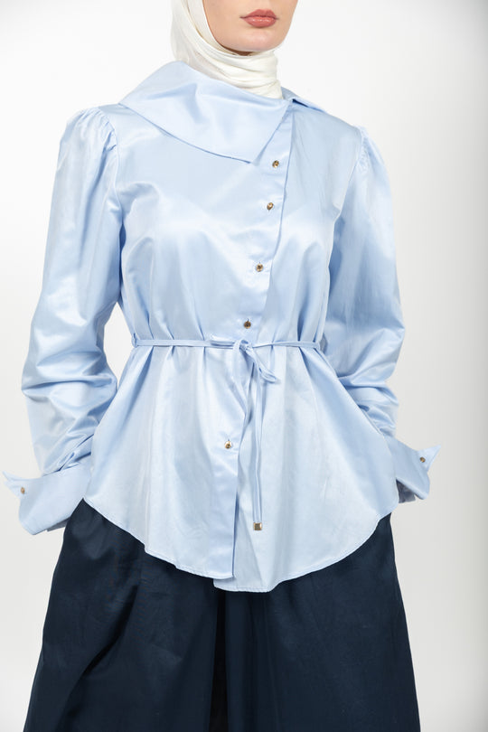 Light blue blouse with a belt and dark pants on a white background