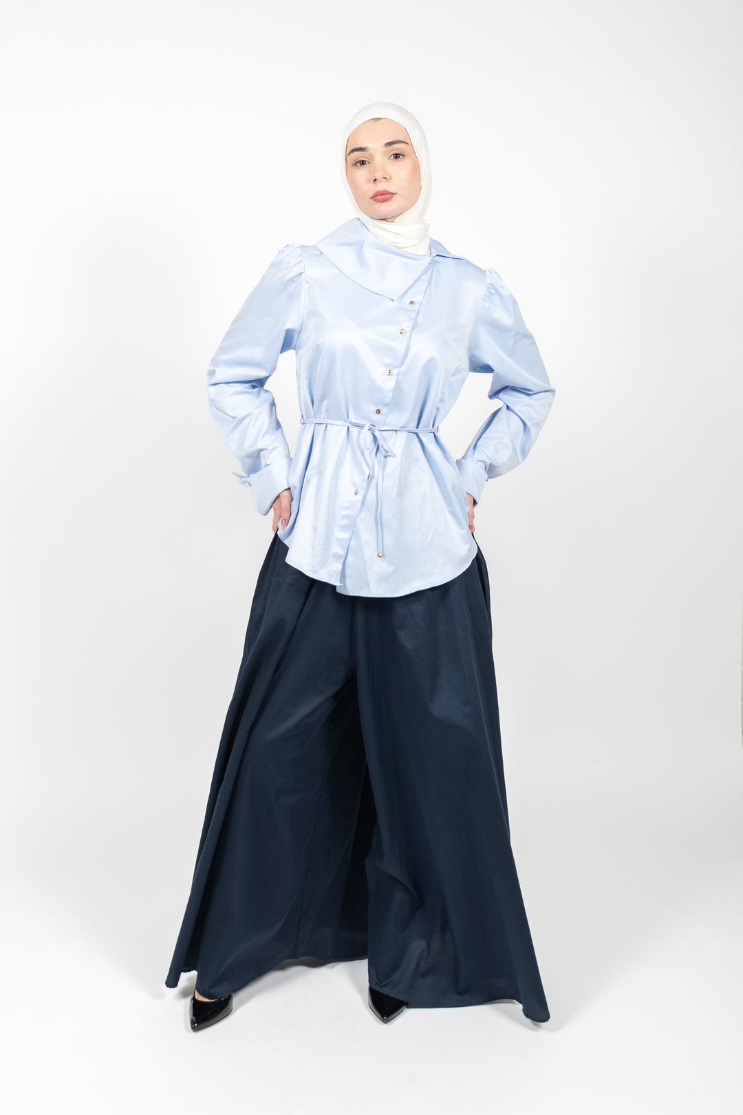 Woman wearing a light blue patterned top and dark navy pants on a white background