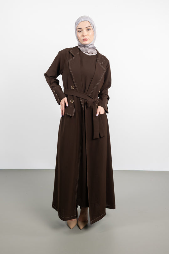 Woman wearing a long brown coat and hijab on a white background