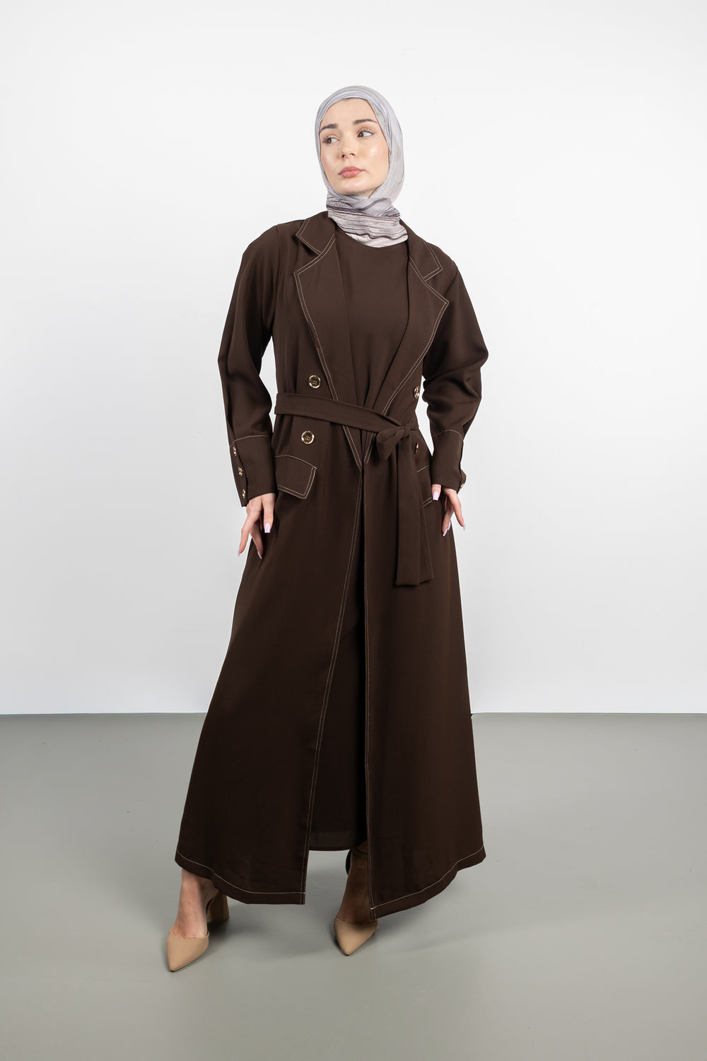 Woman wearing a long brown coat and hijab on a white background