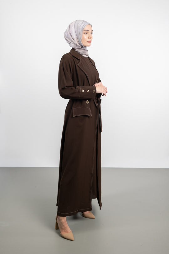 Woman wearing a long brown coat and headscarf on a white background