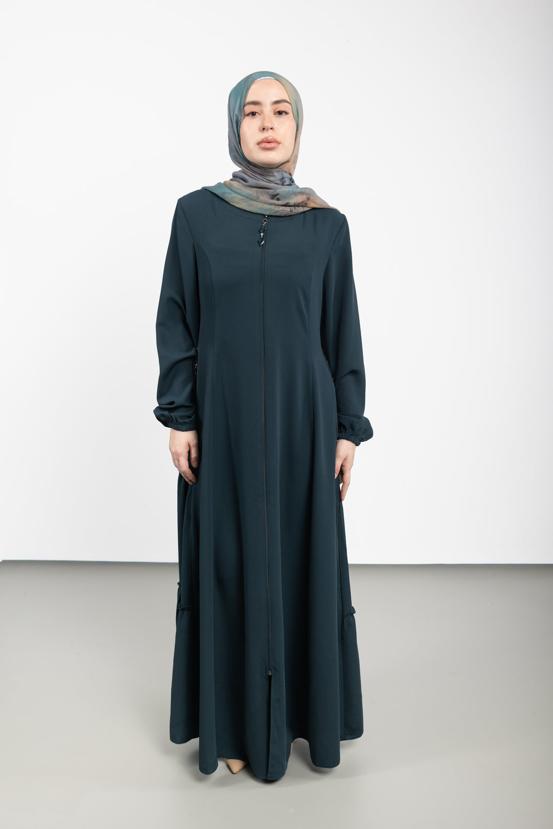 Woman wearing a long dark green Abaya and headscarf on a white background