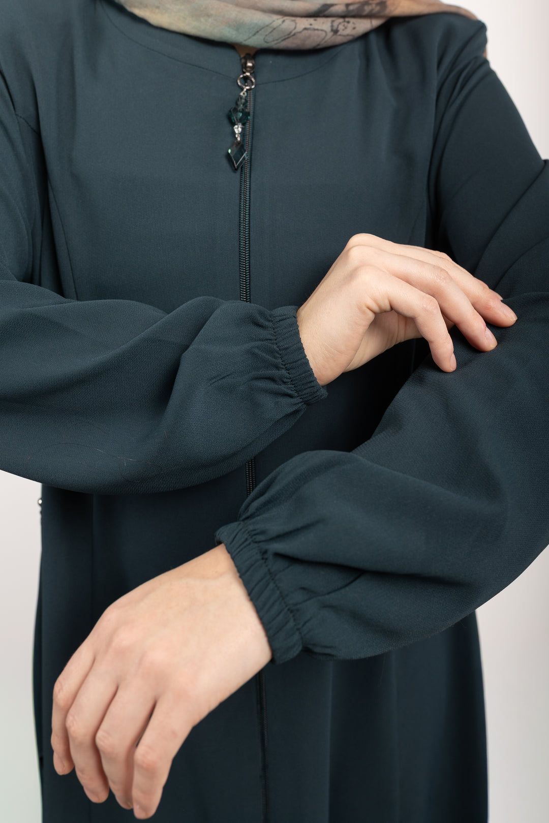 Person wearing a dark green long-sleeve garment with a neutral background