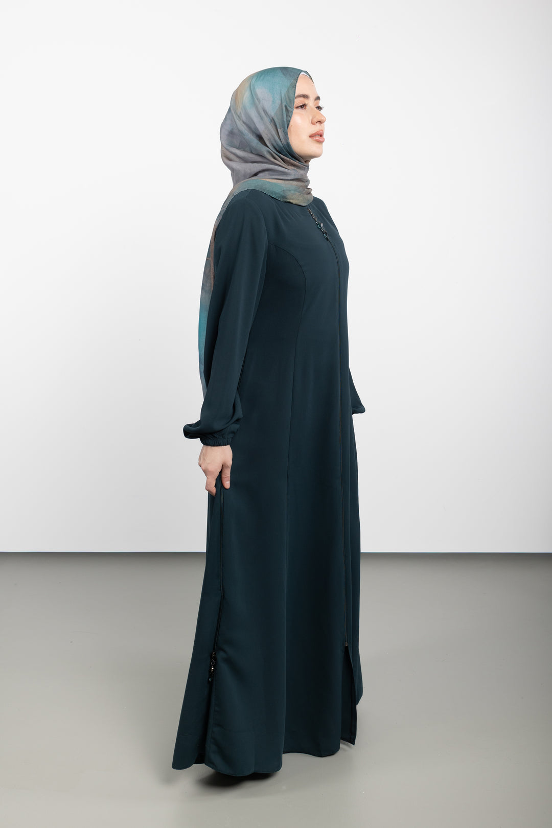 Woman wearing a long dark green dress and light blue hijab on a white background