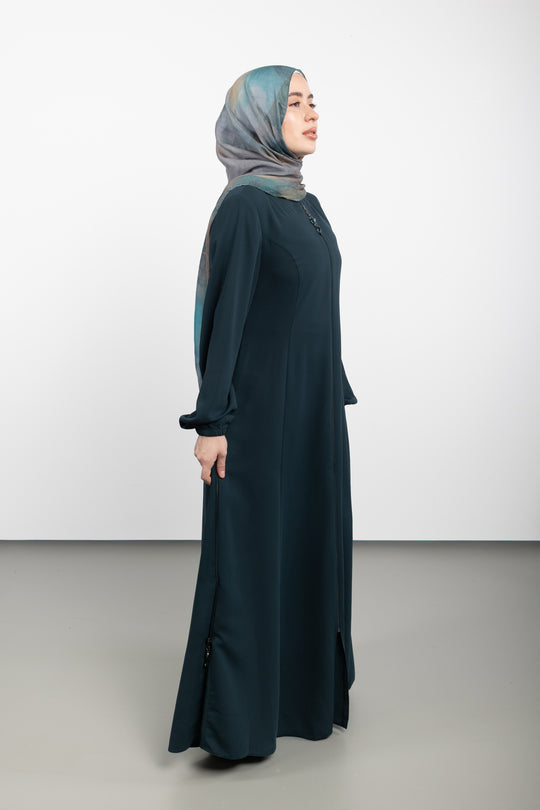Woman wearing a long dark green dress and light blue hijab on a white background