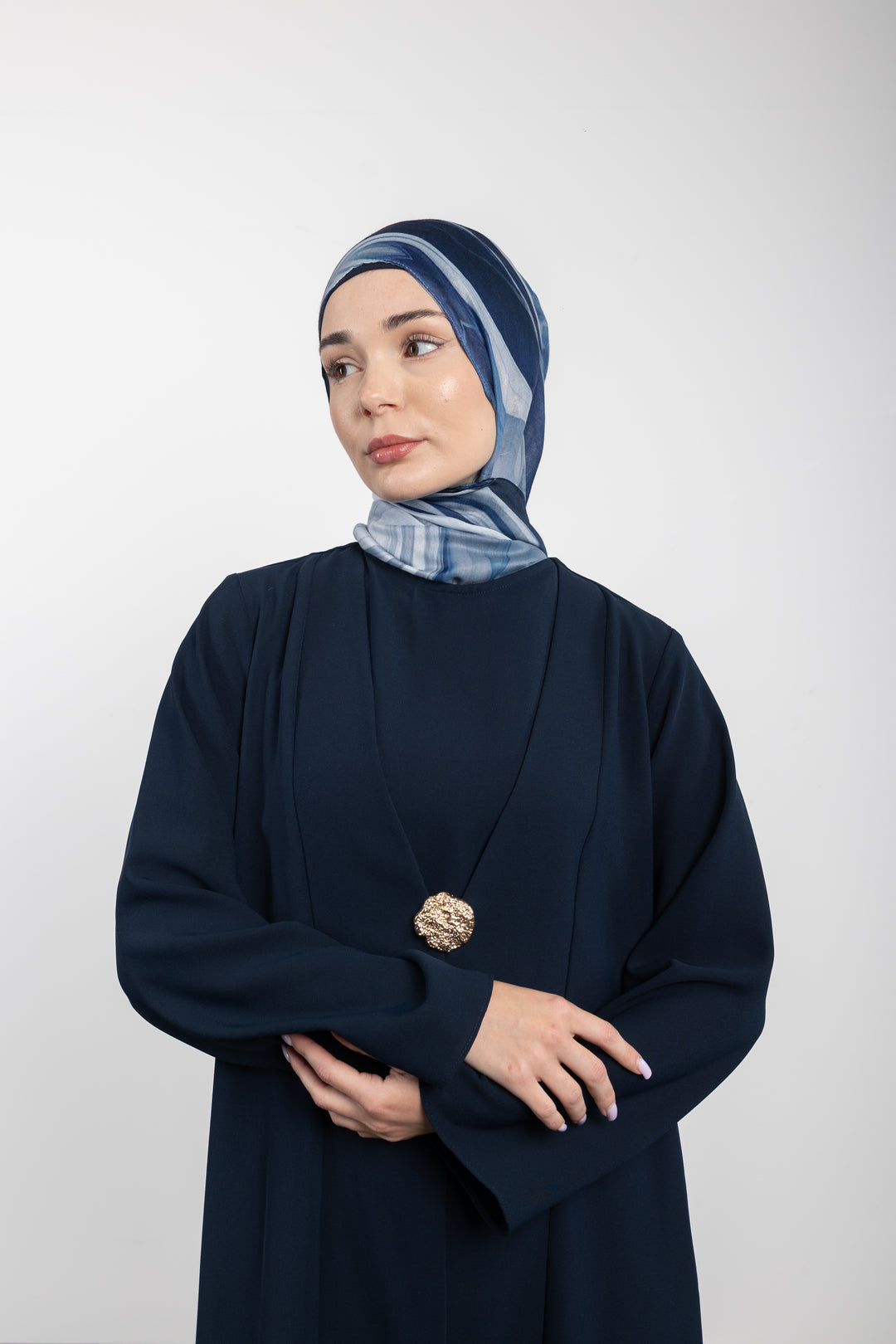 Woman wearing a dark blue outfit with a patterned headscarf against a white background