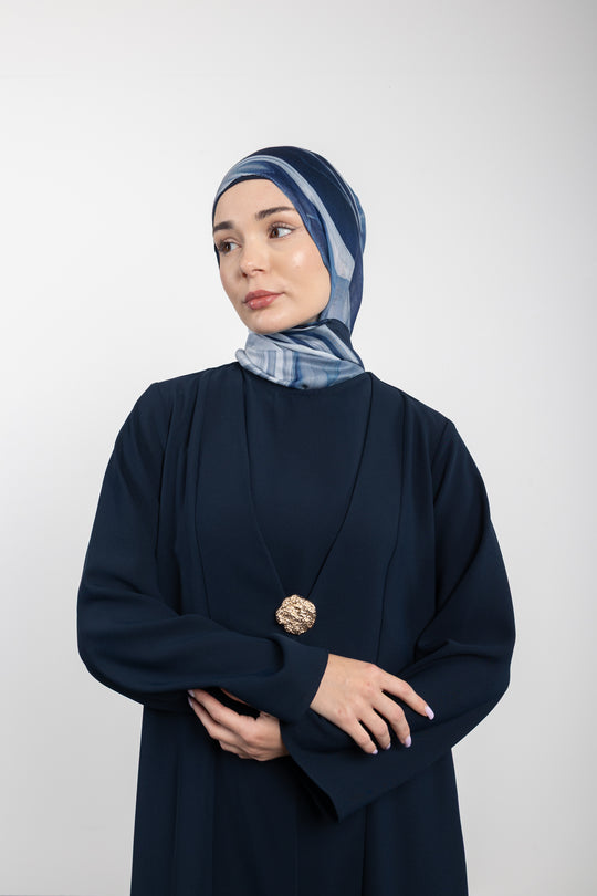 Woman wearing a dark blue outfit with a patterned headscarf against a white background