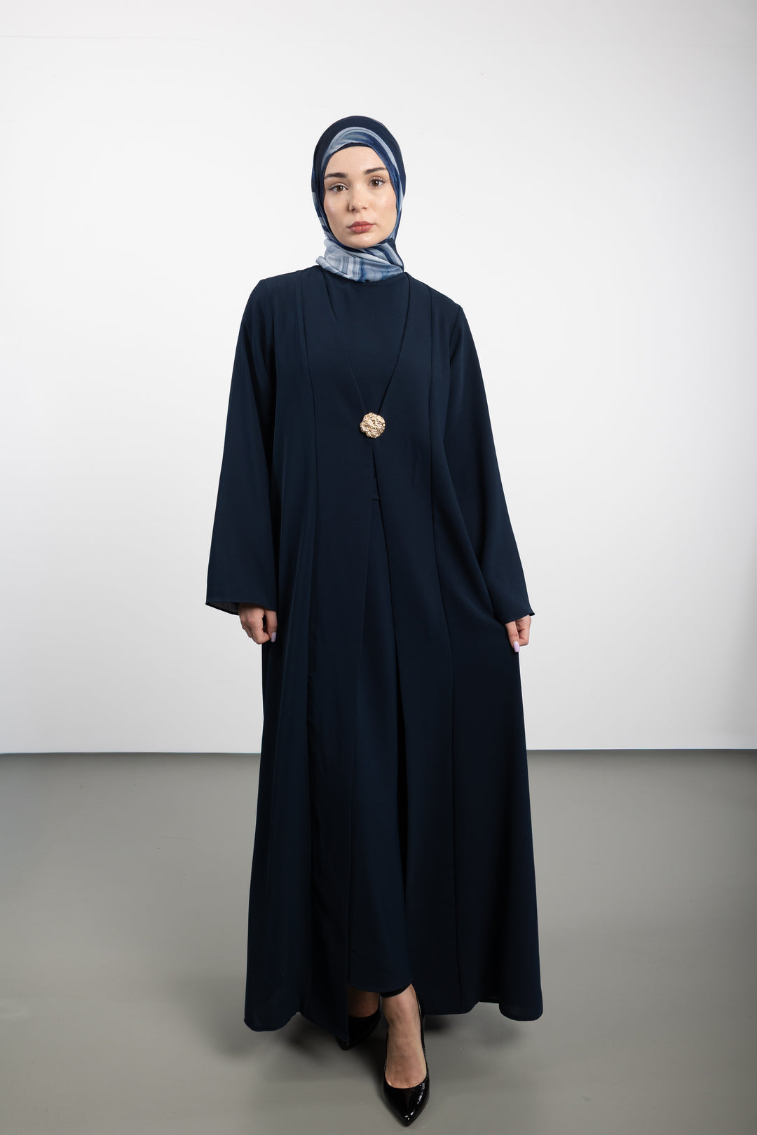 Woman wearing a long dark blue dress with a matching hijab on a white background