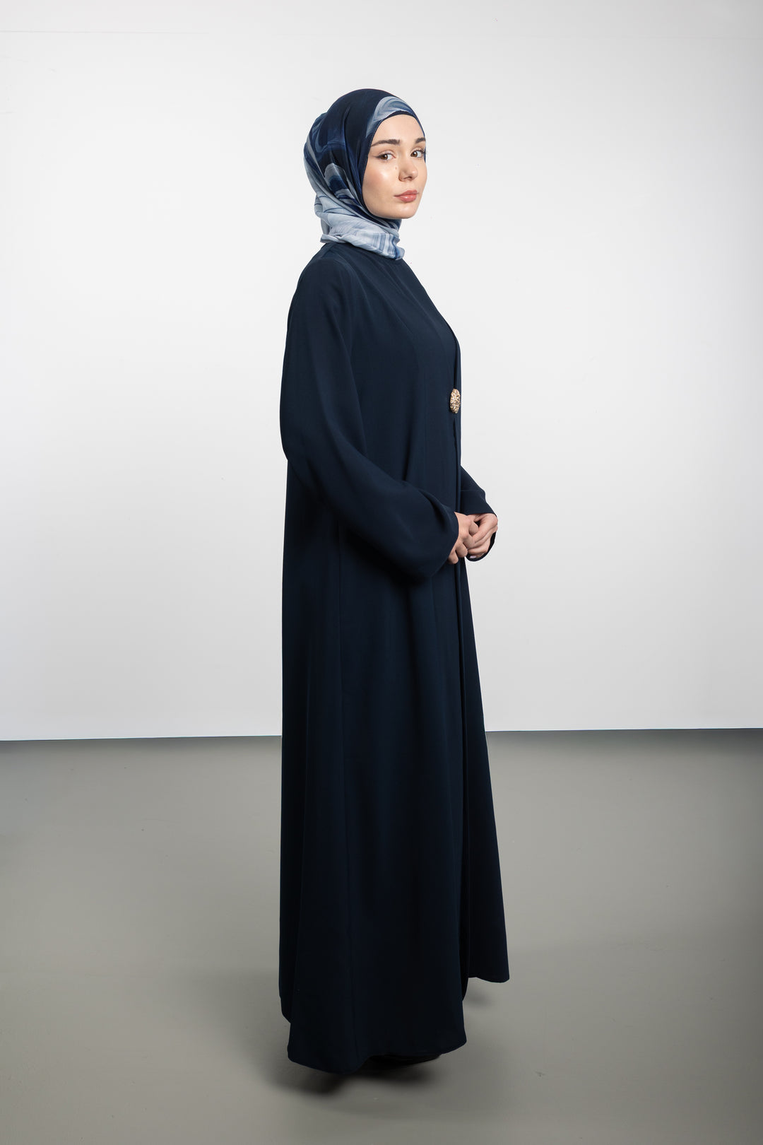 Woman wearing a long dark blue dress and headscarf on a white background