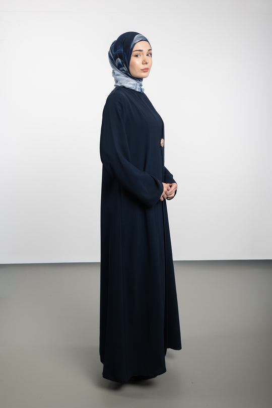 Woman wearing a long dark blue dress and headscarf on a white background