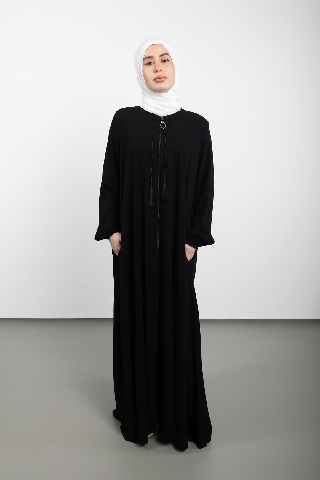 Woman wearing a black abaya with a white hijab on a white background