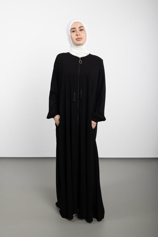 Woman wearing a black abaya with a white hijab on a white background