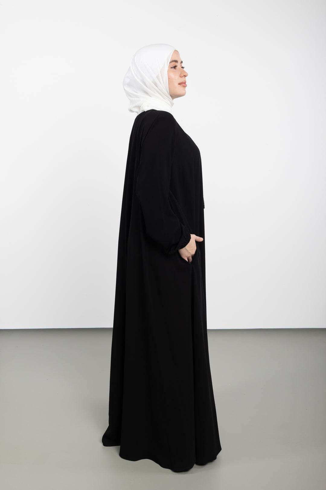 Person wearing a black abaya and white hijab standing against a white background